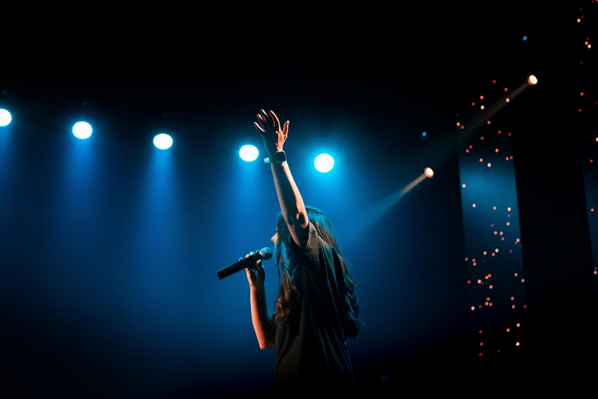Vocalist performing live on a blue-lit stage with a handheld microphone