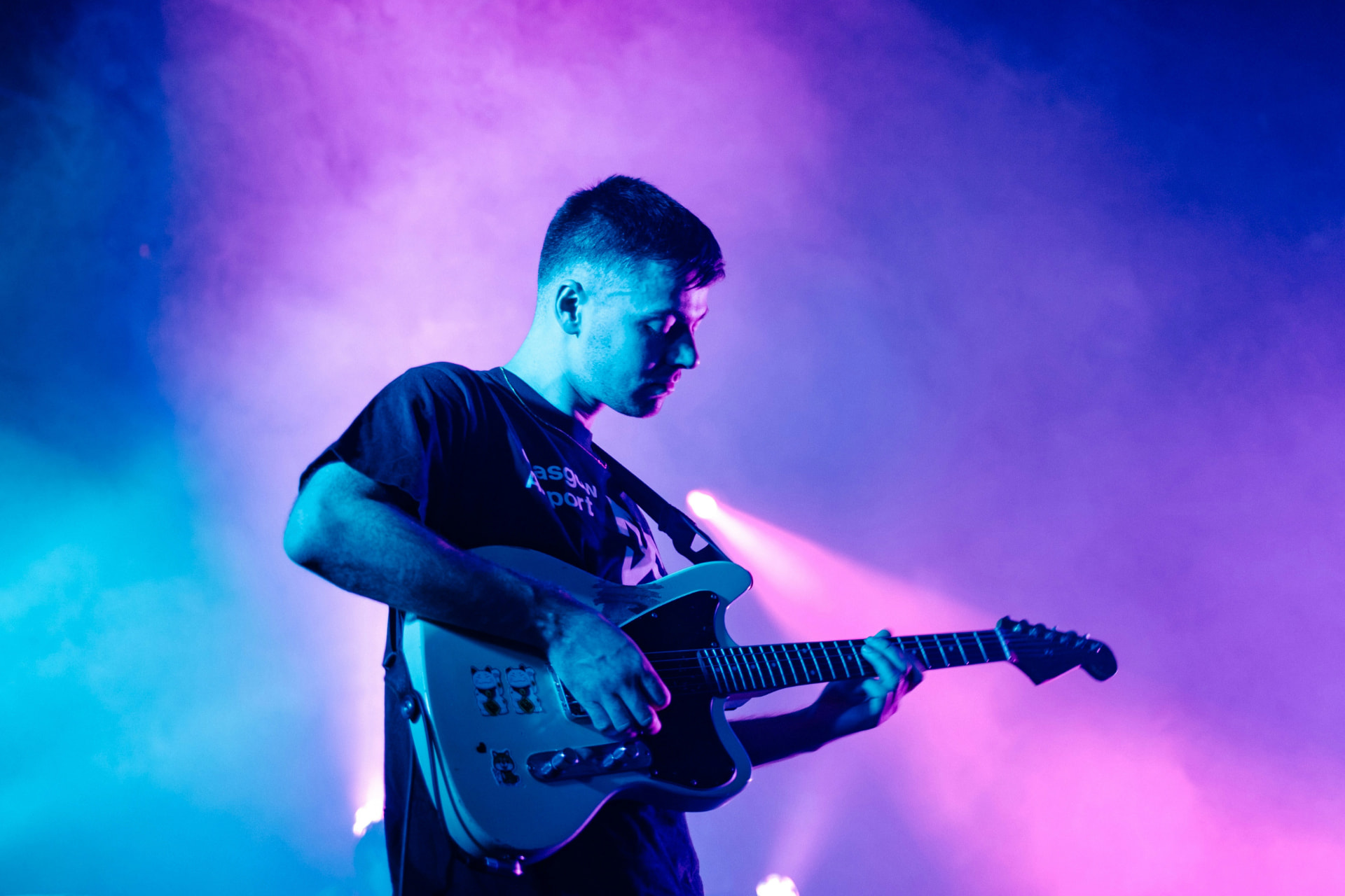 Guitarist performing live under vibrant neon stage lighting